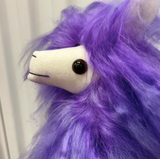 Close-up of a purple llama plush toy with a fluffy shaggy purple mane, a white snout, and a dark brown button eye.