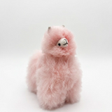 A fluffy pink alpaca plush toy with a small white face, black embroidered eyes and nose, and tiny gray horns, photographed on a clean white studio background.