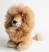 A plush lion toy with a fluffy tan and light brown mane, cream-colored face, and black nose details, posed against a clean white background.