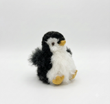A small alpaca plush penguin toy with black and white fur, a yellow beak, and yellow feet, photographed on a clean white studio background.