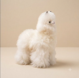 A fluffy white alpaca fur plush toy with small black embroidered eyes and a pink stitched mouth, sitting on a warm beige background.