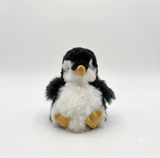 A small alpaca plush penguin toy with black and white fluffy feathers, a yellow beak, and yellow feet, sitting against a plain light gray background.