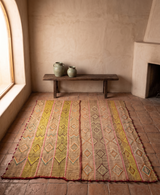Vintage earth-toned Peruvian Frazada wool rug with diamond pattern, sand and green stripes, handcrafted rustic home decor on terracotta floor.