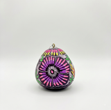 Hand-carved and hand-painted gourd ornament showing a hummingbird's tail feathers in a pink and purple floral pattern against a dark purple background, handmade in Cochas, Huancayo, Peru.