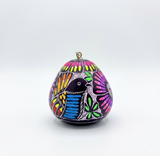 Hand-carved and hand-painted gourd Christmas ornament with a hummingbird's face design in pink, yellow, orange, blue, and green against a dark purple background, handmade in Cochas, Huancayo, Peru.