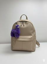 Beige backpack with a purple fluffy charm on a white background