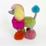 A curated collection of vibrant, multi-color artisan alpaca fur plush toys, including a rainbow poodle, pastel lion, and stuffed teddy bear on a clean neutral backdrop. An editorial text overlay highlights unique, handmade heritage gifts from Peru