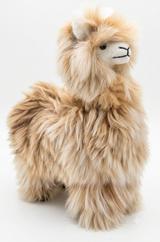 A fluffy alpaca plush toy with long tan and cream fur, a white face, and small black embroidered facial features, photographed on a clean white background.