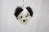 A handmade alpaca fur keychain in the shape of a panda bear, predominantly white with black ears, nose, and eyes.