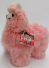 A pink stuffed alpaca toy with a tag indicating 'Peru'.
