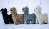 A set of four felted alpaca yarn ornaments in black, brown, gray, and white, displayed in a row.