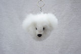 Handmade white alpaca fur keychain shaped like a bear with black eyes and nose, displayed against a grey background.