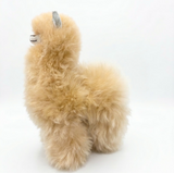 A fluffy alpaca plush toy in a light tan color, shown from a side profile against a plain white background.