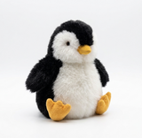 A plush alpaca  toy penguin with black and white fur, a yellow beak, and yellow feet, sitting against a seamless white background.