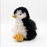 An alpaca fur plush toy penguin with black and white fluffy feathers and a yellow beak and feet, sitting on a plain white background.