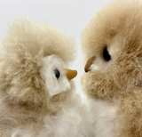 Close-up of two alpaca fur owl stuffed animals facing each other, showing the natural texture and beak detail