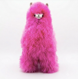 A bright pink fluffy alpaca plush toy with a white face and small brown ears, photographed against a clean white studio background.