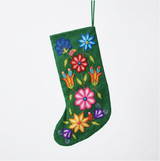 A green velvet Christmas stocking decorated with colorful hand-embroidered flowers in pink, blue, red, orange, yellow, and purple, hanging against a plain white background.