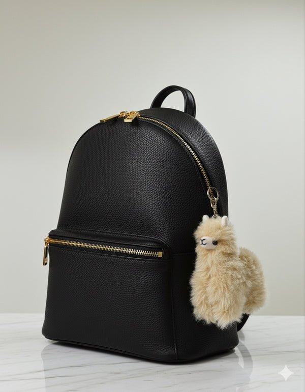 Black backpack with a fluffy beige llama charm on a light gray background