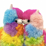 Two plush alpaca toys with fluffy rainbow-colored fur and small white horns, posed facing each other on a plain white background.