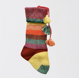 A colorful striped knit Christmas stocking with three hanging tassels, shown against a plain light gray background.