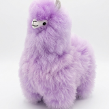 A fluffy lavender alpaca plush toy with a small white and black face, photographed against a seamless white studio background.