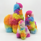Three fluffy alpaca fur plush toys in different sizes, each covered in rainbow-colored alpaca fur with pink, blue, yellow, green, orange, and purple sections, photographed on a clean white studio background.