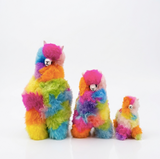 Three fluffy alpaca plush toys in different sizes, each covered in a bright rainbow patchwork pattern of pink, blue, yellow, green, and orange, set against a plain white background.