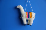 Knitted llama ornament with a colorful saddle on a blue background