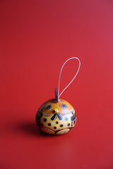 A hand-carved and hand-painted gourd ornament with a design resembling a chicken, displayed against a red background.