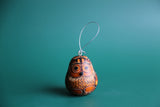 A handmade natural gourd ornament painted to resemble an owl, with a silver hanging loop.