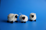 Three hand-knitted alpaca yarn sheep ornaments with white curly wool texture and black knitted faces and legs, handmade in the Andes of Peru