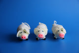 Three hand knitted pig ornaments with white bodies and pink noses, displayed against a blue background.