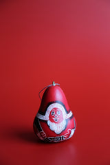 A hand-carved and hand-painted red ornament in the shape of a Santa Claus figure, with black outlines and a festive design, placed against a red background.
