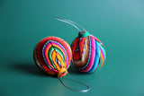 Two colorful spherical ornaments with geometric patterns, made of fabric, displayed against a green background.